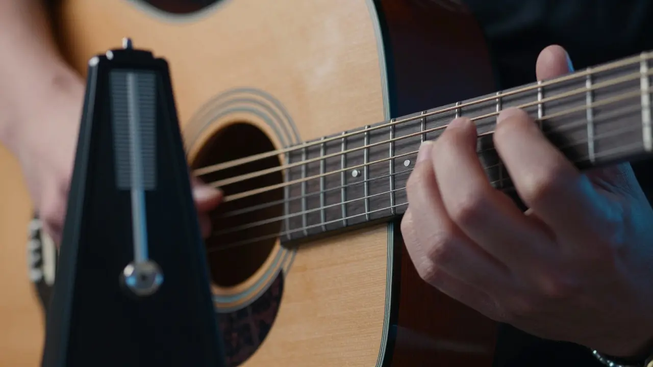 Fingers changing chords on a guitar with a metronome in the background